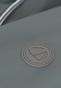 Gray silicone bag detail featuring a circular logo patch with a sailboat design, accompanied by a contrasting striped zipper.