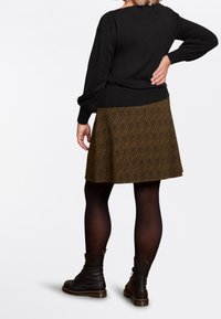 Svart sweater och brun kjol med lövmönster, med knähöga svarta lace-up stövlar. Kjolen har en utfläkt form och texturerad tyg.