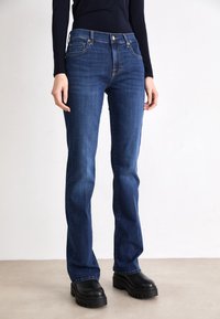 Dark blue denim jeans with a straight leg design, featuring a mid-rise waist, front pockets, and gold hardware accents.