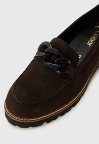 Braune Wildleder-Slipper mit einem schwarzen strukturierten Kettenakzent, genähten Details und einer Gummisohle für Gripp. Klassische, runde Form.