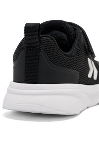 Zwarte sportieve schoen met een bovenwerk van mesh, textuurdetails en een verstelbare band. Beschikt over een witte rubberen zool en een lus aan de hiel.