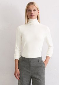 Witte coltrui gemaakt van een gladde stof, met lange mouwen. Gepaard met grijze pantalon met een streeppatroon.