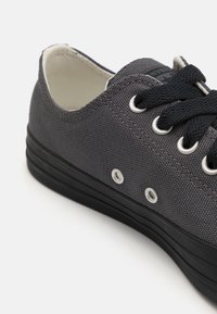 Szare płócienne trampki o teksturowanym wykończeniu, czarne sznurowadła i srebrne oczka. Posiadają czarną gumową podeszwę i lekko podniesioną konstrukcję.