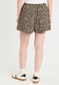 Shorts imprimé léopard avec une taille élastique, dans des couleurs beige et noir. Le matériau semble léger et respirant. Portés avec des baskets décontractées.