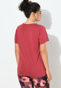 Czerwony t-shirt z krótkim rękawem o luźnym kroju i gładkiej fakturze. Noszony z czarnymi legginsami z kwiatowym wzorem w odcieniach różu i fioletu.