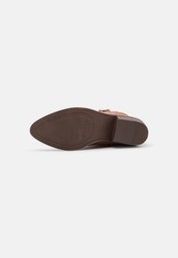 Chaussure en cuir marron avec une semelle texturée, dotée d'un talon bas et d'un accent boucle. Vue du dessous montrant un motif rainuré pour une meilleure adhérence.