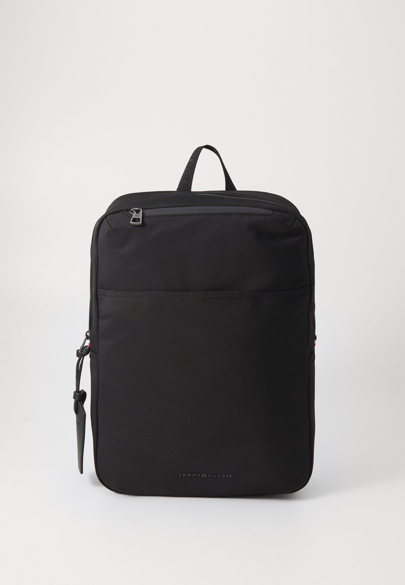 Zwarte rugzak met een slank design, gemaakt van duurzaam fabric, voorzien van een handvat aan de bovenkant, een ritsvak aan de voorkant en het logo van Tommy Hilfiger.