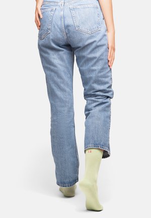 Light blue denim jeans with a relaxed fit, featuring a high waist and standard pockets. Worn with light green socks with a small logo.