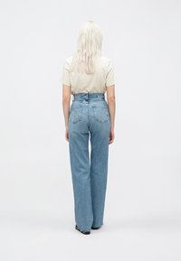 Vaqueros de tiro alto de color azul claro con corte de pierna amplia, que cuentan con dos bolsillos traseros y una tela sutilmente texturizada. Combinados con una camiseta beige.