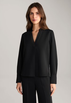 Blusa nera a maniche lunghe con scollo a V e una linea dritta. Realizzata in tessuto morbido con una leggera lucentezza. Design minimalista, senza motivi visibili.