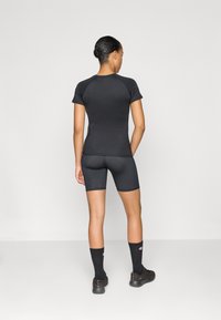 Svart träningslinne med korta ärmar, kombinerat med figurnära svarta shorts. Båda plaggen har en slät textur och minimala design detaljer.