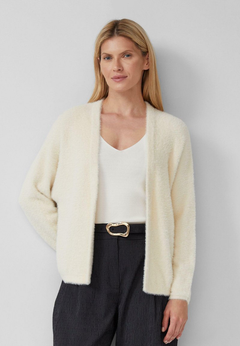 Fuzzy crèmekleurige cardigan met open voorkant, lange mouwen en geribde manchetten, gecombineerd met een witte v-hals top en hoge taille pinstripe broek.