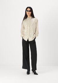 Camicia dorata con paillettes, colletto, maniche lunghe e chiusura con bottoni, abbinata a pantaloni neri a gamba larga e stivaletti neri.