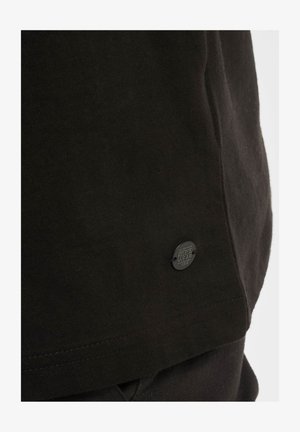 Černé bavlněné tričko s vroubkovaným výstřihem a postranním švem. Obsahuje malou černou štítek Roca Wear blízko lemu.