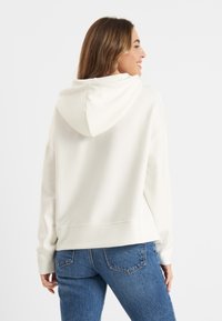 Witte hoodie met een relaxed fit, voorzien van lange mouwen en een cropped ontwerp. Zachte stof en een geribbelde zoomafwerking. Geshowde spijkerbroek.