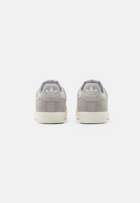Sneakers in suede grigio con suole in gomma bianca, dotate di un logo tonale sul tallone e dettagli testurizzati sulla suola. Vista posteriore.