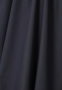 Tissu bleu marine foncé avec des plis doux et une texture lisse et mate suspendu verticalement.