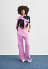 Μαύρο τοπ από διχτυωτό ύφασμα με λευκές λεπτομέρειες και ροζ φόρμα. Το παντελόνι έχει φαρδιά εφαρμογή, είναι από απαλό ύφασμα και φέρει το λογότυπο "nike".