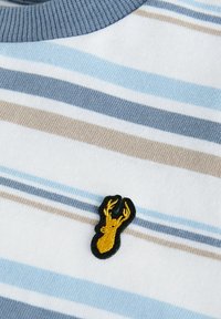 Ribaga lühikeste varrukatega särk valgetes, sinistes ja beežides triipudes. Rinnal on must ja kuldne tikandiga hirve logo. Pehme puuvillane materjal.