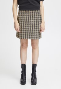 Jupe en motif pied-de-poule en tissu beige et noir, coupe droite, longueur mi-thigh, portée avec des bottines noires élégantes.