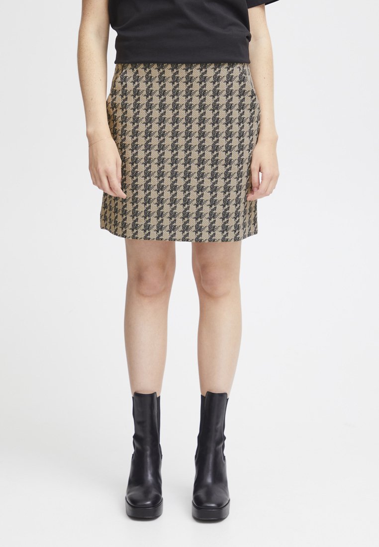 Jupe en motif pied-de-poule en tissu beige et noir, coupe droite, longueur mi-thigh, portée avec des bottines noires élégantes.