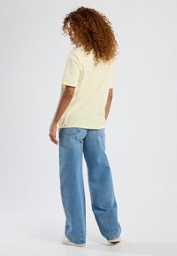 Pale yellow, short-sleeve t-shirt paired with light blue, wide-leg jeans. Front pocket detail visible on jeans. Plain background.