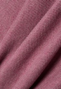Close-up van opgevouwen roze gebreide stof die de gedetailleerde textuur en weefpatroon toont.