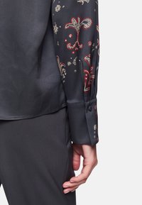 Silky dark gray shirt with intricate floral and abstract patterns in red and cream. Features buttoned cuffs and a smooth texture.