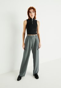 Čierny bezramienkový crop top s vysokým golierom, skombinovaný so šedými širokými cargo nohavicami s bočnými vreckami a hladkou textúrou.