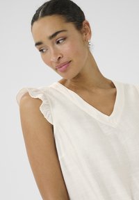 Blouse crème à col en V avec des manches courtes volantes, dotée d'un tissu léger et texturé et d'une coupe décontractée.