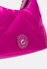 Różowa pikowana torebka wykonana z błyszczącego materiału, z okrągłą srebrną naszywką logo oraz czarnym zamkiem błyskawicznym z metalowymi akcentami.