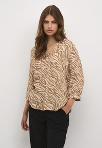 Beige und hellbraun gestreifte Bluse mit V-Ausschnitt, dreiviertel �Ärmeln und lockerer Passform, kombiniert mit schwarzen Hosen.