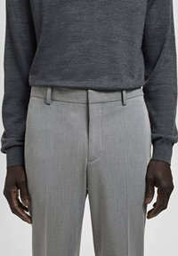 Szare, dopasowane spodnie wykonane z lekkiego materiału, posiadające płaskie przody, dwie boczne kieszenie oraz wąski krój.