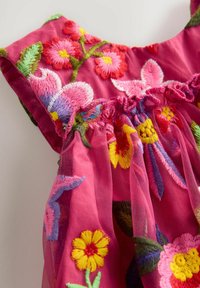 Close-up af lyserødt stof med flerfarvet blomsterbroderi i gul, rød, lilla og grøn på samlet, gennemsigtigt materiale.