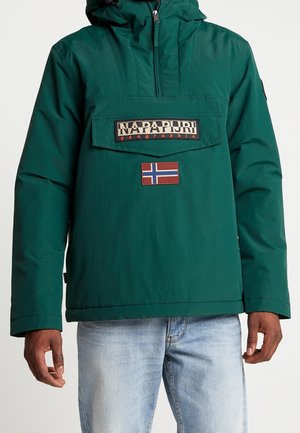 Bluza pulower w kolorze zielono-niebieskim z przednią kieszenią z klapką oznaczoną napisem „Napapijri geographic” oraz naszywką z flagą Norwegii, noszona z jasnoniebieskimi dżinsami.