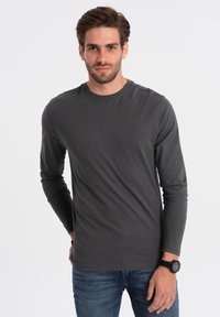 Langarmshirt met ronde hals in donkergrauwe stof, met een gladde textuur en een aansluitend ontwerp. Draagt met blauwe jeans en een zwart horloge.