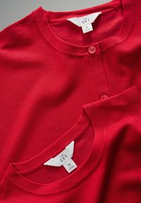 Rode gebreide cardigans gestapeld, met ronde neksnoeren en knoopsluitingen. Labels zichtbaar, die maat medium en merk "THE SET" aangeven.
