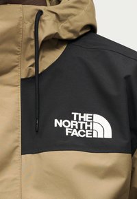 Μπεζ και μαύρο μπουφάν με κουκούλα, με φερμουάρ μπροστά και ορατό λογότυπο σε λευκό στην περιοχή του στήθους. Ομαλή υφή, ελαφρύ υλικό.