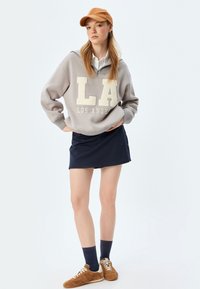 Szary sweatshirt z napisem "LA" w kolorze kremowym, zestawiony z granatową mini spódnicą. Dodatki to jasnobrązowa czapka i tanowe sneakersy.