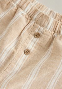 Short beige clair avec des rayures verticales blanches, doté d'une taille élastique froncée et de deux boutons décoratifs marron à l'avant.