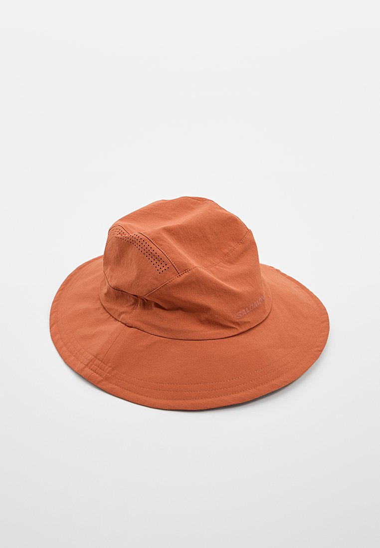 Sombrero de ala ancha color óxido hecho de un tejido ligero con perforaciones de ventilación y un sutil texto de la marca "Salomon" en un lado.