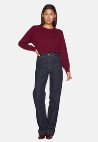 Maglione borgogna con scollatura rotonda e maniche a raglan, abbinato a jeans blu scuro a vita alta con cuciture a contrasto e bottone frontale.