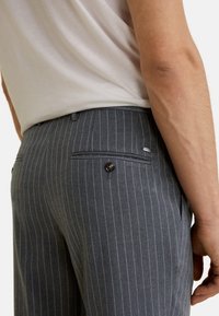 Pantalones grises a rayas finas, hechos de un material suave. Cuentan con un bolsillo trasero con cierre de botón y una pequeña etiqueta de tela en la cinturilla.