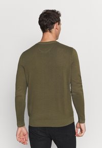 Pull en tricot vert olive avec des manches longues, un col rond, une texture côtelée subtile et une coupe ajustée. La vue arrière montre une finition sans couture.