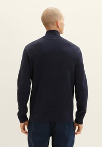 Marineblaues strukturiertes Strickpullover mit hohem Kragen, langen Ärmeln und gerippten Bündchen. Keine sichtbaren Logos oder Muster auf der Rückseite.