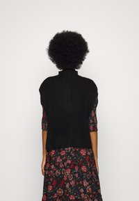 Haut sans manches en tricot noir avec un col montant, associé à une robe à motif floral avec des manches courtes et un ourlet à volants.