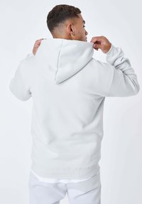 Felpa con cappuccio grigio chiaro dal taglio comodo. Il materiale sembra morbido, con polsini a coste. Sul retro presenta un cappuccio a punta e cuciture visibili.