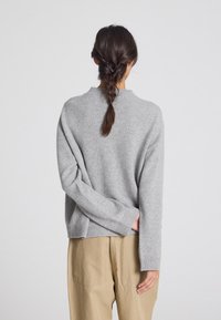 Maglione grigio chiaro con polsini e orlo a coste, caratterizzato da una vestibilità ampia e una texture sottile. Abbinato a pantaloni color khaki.
