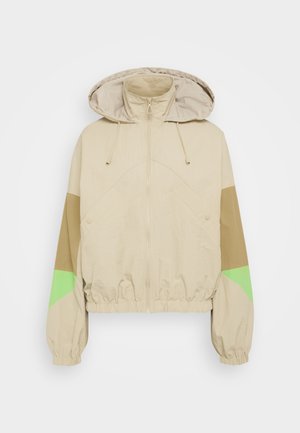Veste à capuche beige avec taille et poignets élastiques. Présente des accents de panneaux vert et marron sur les manches. Tissu léger et texturé.