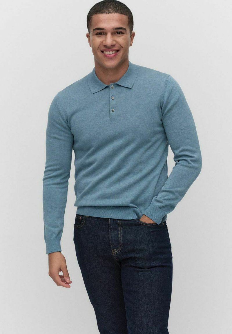 Ljusblå långärmad polo med krage och tre knappar, kombinerad med mörkblå jeans. Tyget ser mjukt och slätt ut.